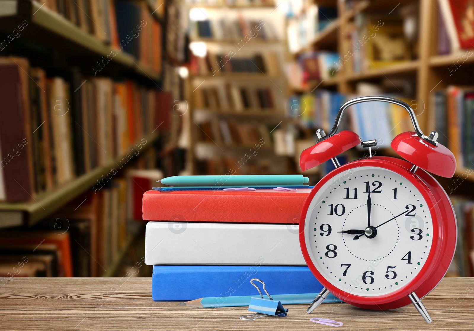 Image of Red alarm clock and different stationery on wooden table in library