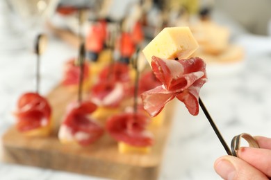 Photo of Woman holding tasty canape with cheese and prosciutto on table, closeup. Space for text