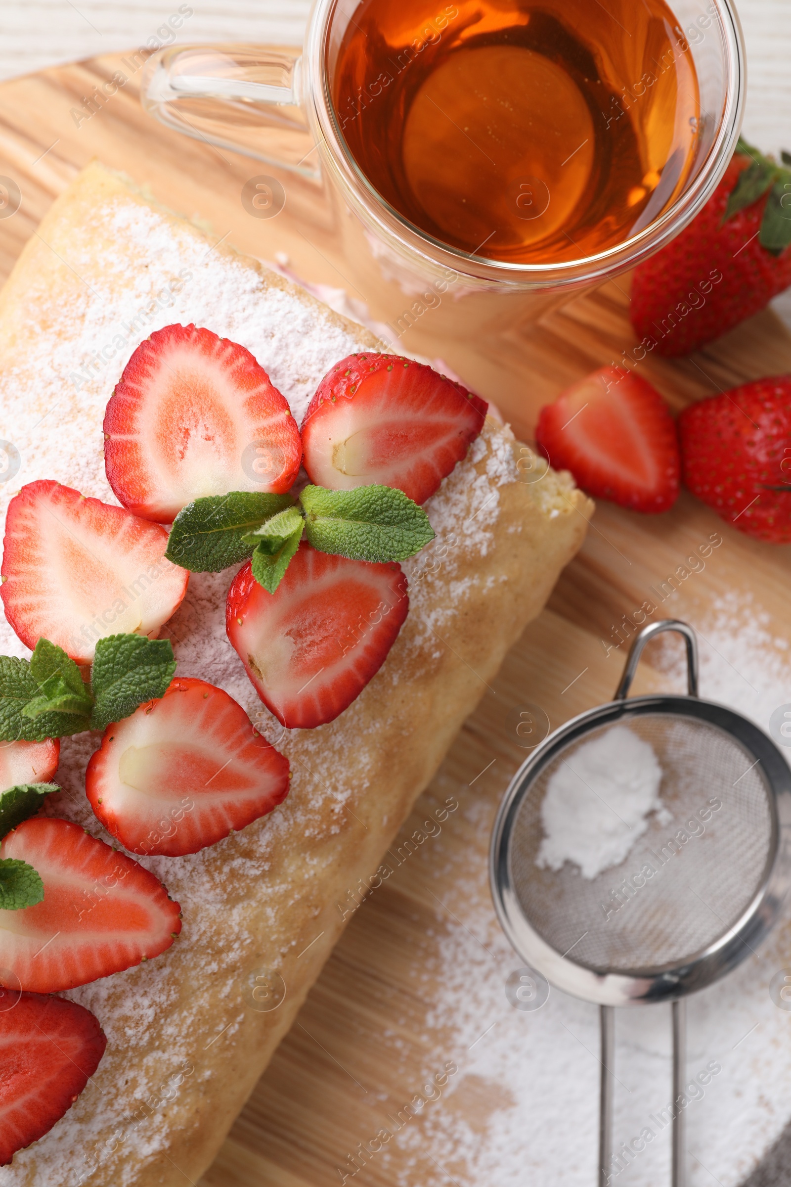 Photo of Delicious cake roll with strawberries and tea on table, flat lay