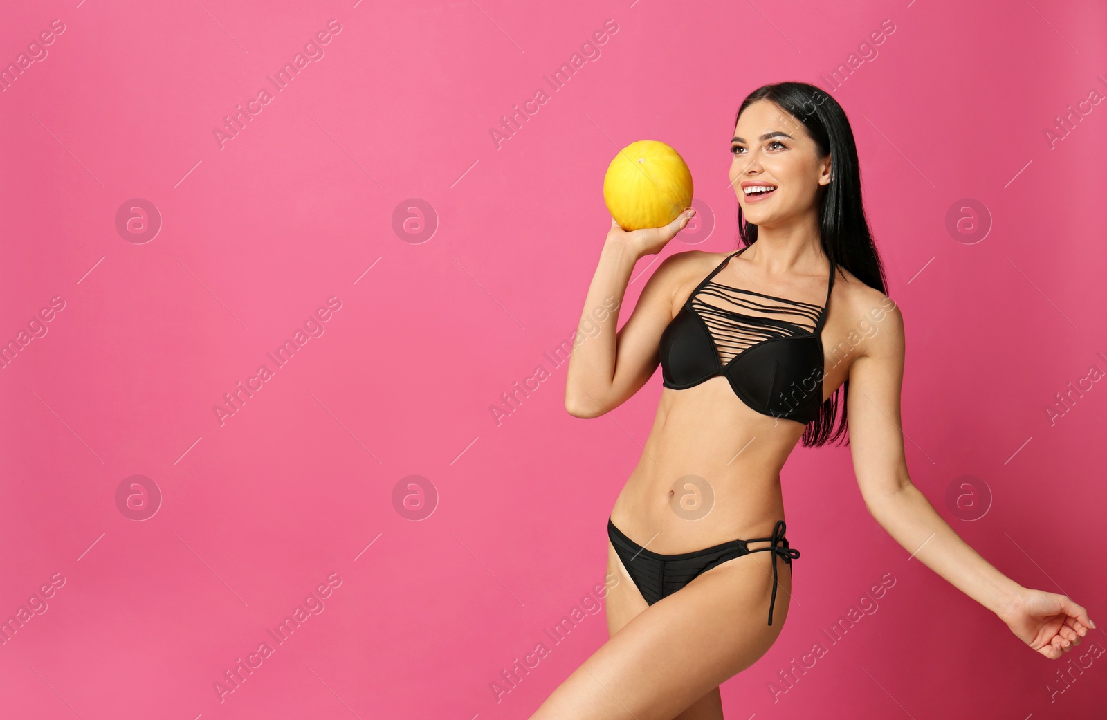 Photo of Beautiful young woman in black bikini with melon on pink background. Space for text