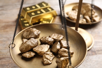 Scale pan with gold lumps on wooden table, closeup