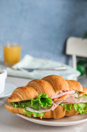 Tasty croissant sandwich with ham and cucumber on light table