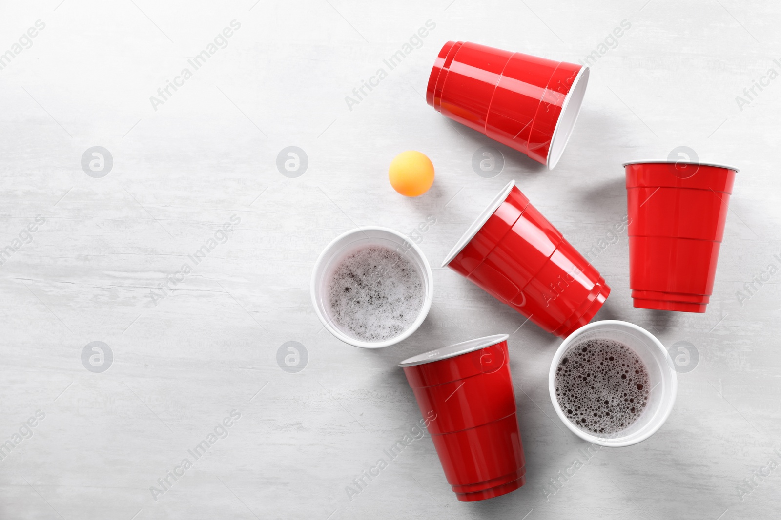 Photo of Plastic cups and ball on white table, flat lay with space for text. Beer pong game