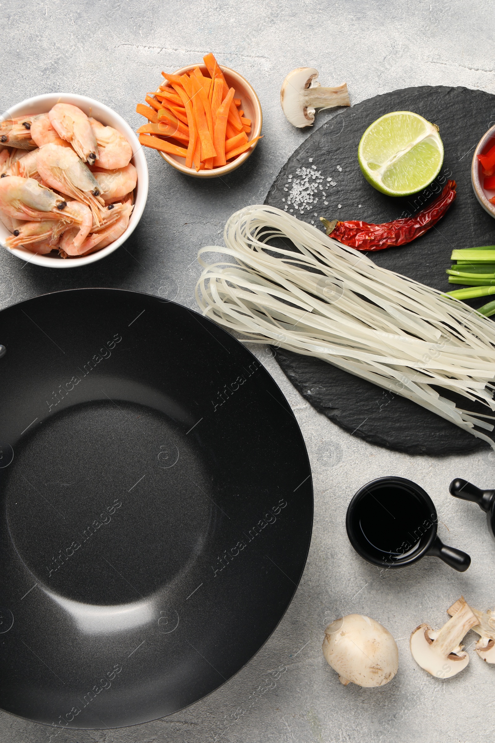 Photo of Flat lay composition with black wok, spices and products on grey textured table