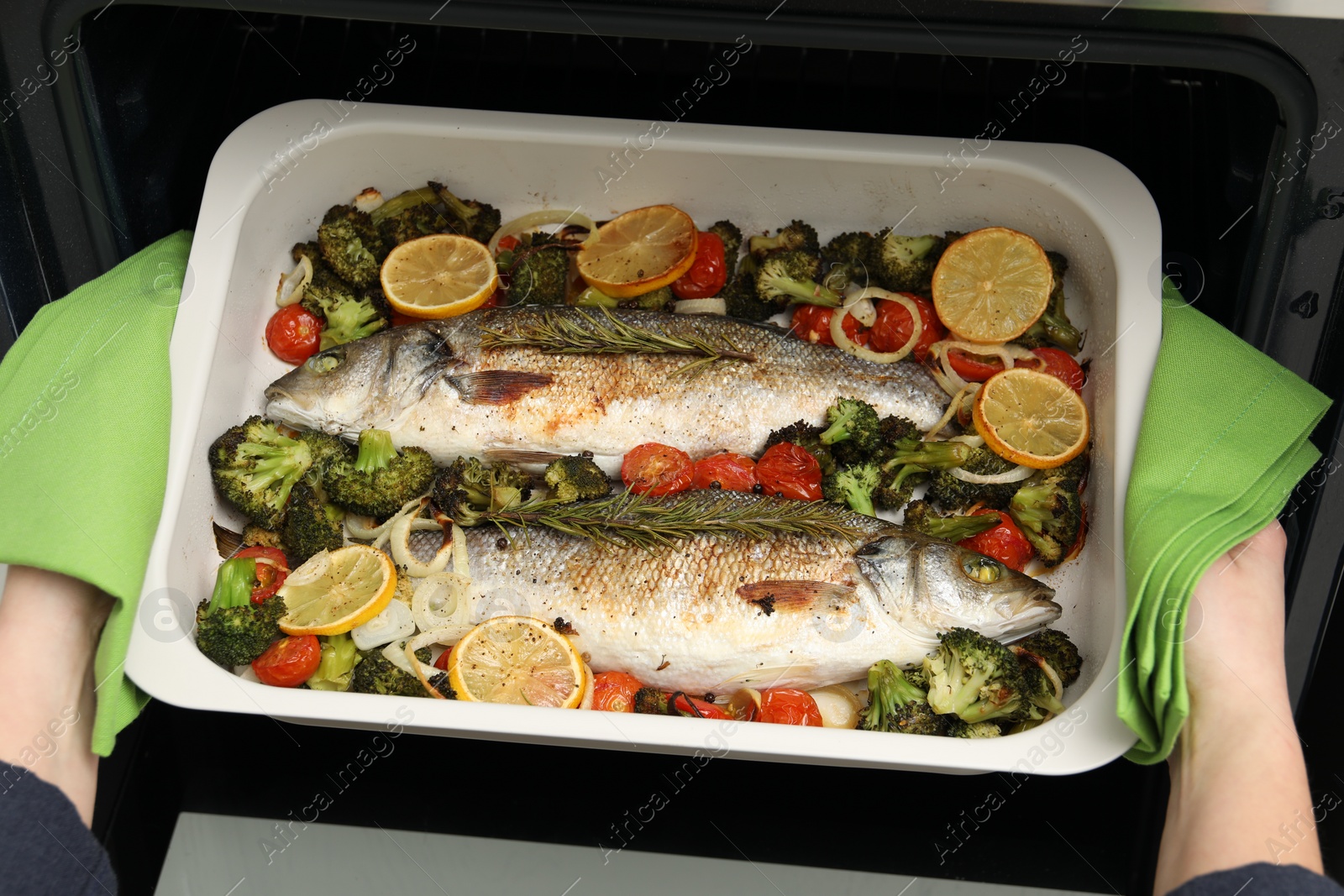 Photo of Woman taking baking dish with delicious fish and vegetables from oven, top view