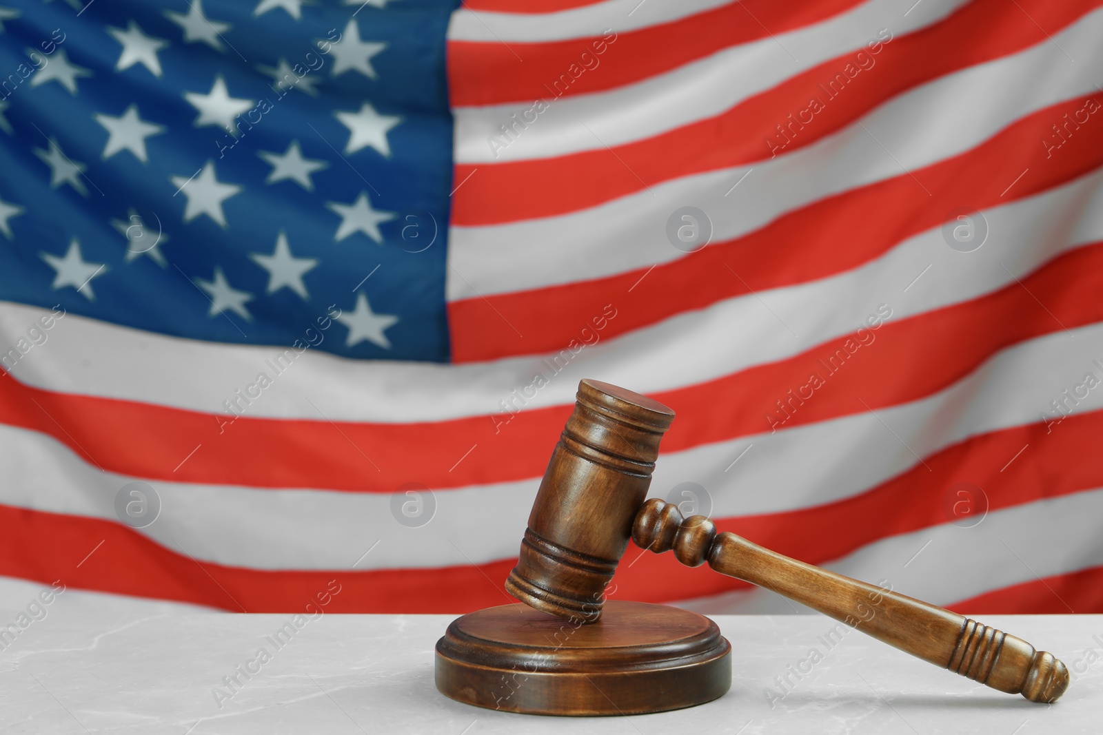 Photo of Wooden gavel on light grey table against American flag. Space for text
