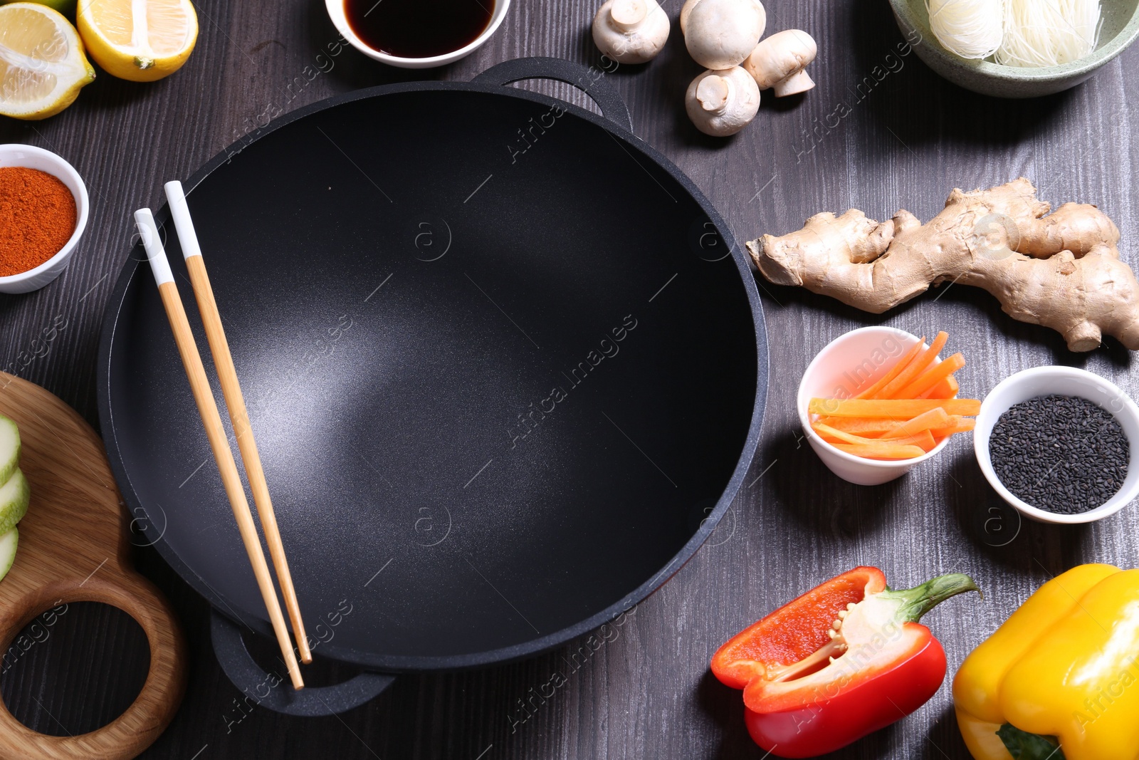 Photo of Empty iron wok, chopsticks and ingredients on dark grey wooden table, above view