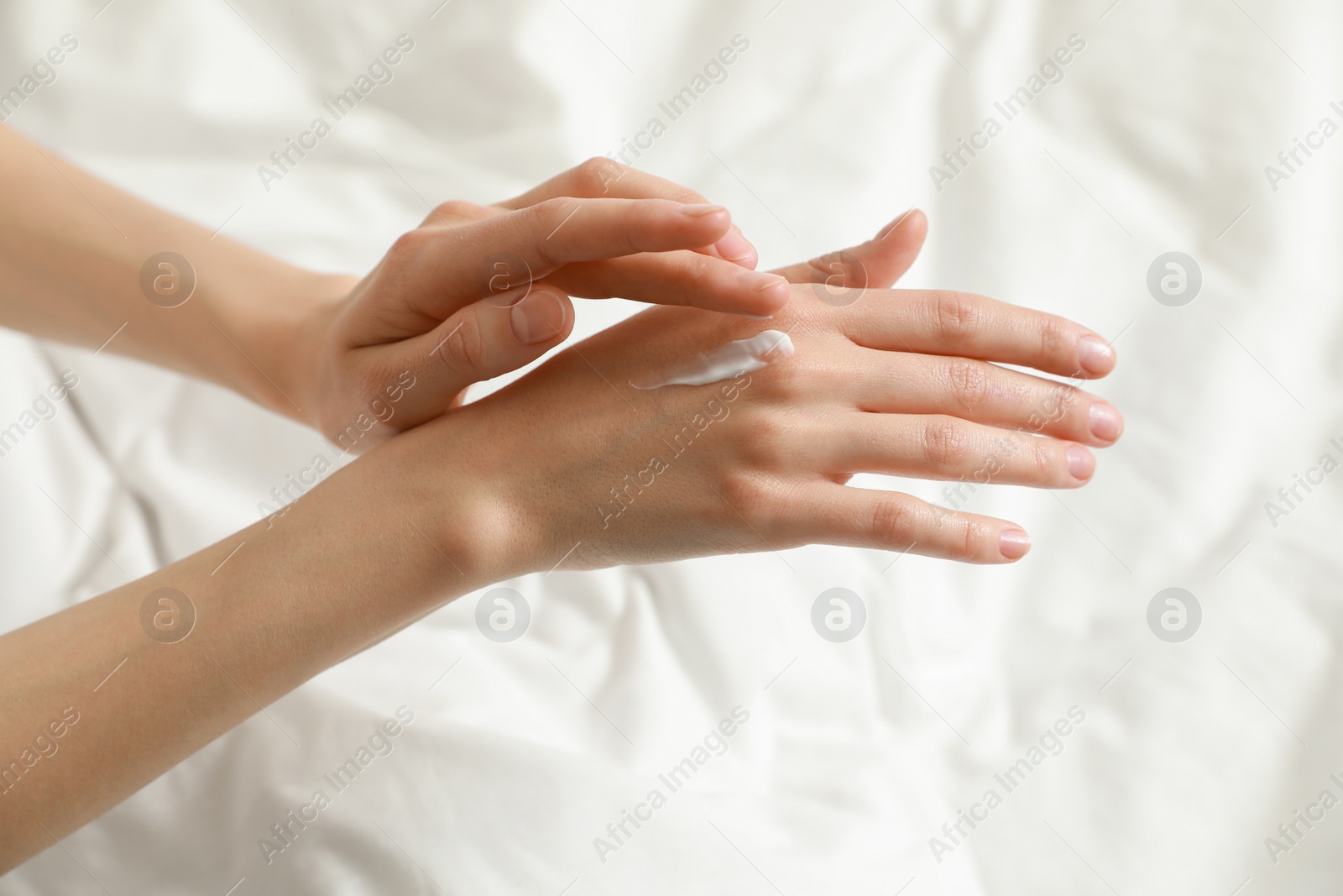 Photo of Woman applying hand cream in bed, closeup