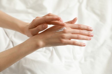 Woman applying hand cream in bed, closeup