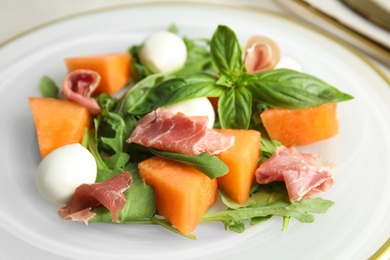 Photo of Fresh melon with prosciutto, mozzarella and basil on plate, closeup