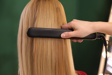 Photo of Stylist straightening woman's hair with flat iron in salon