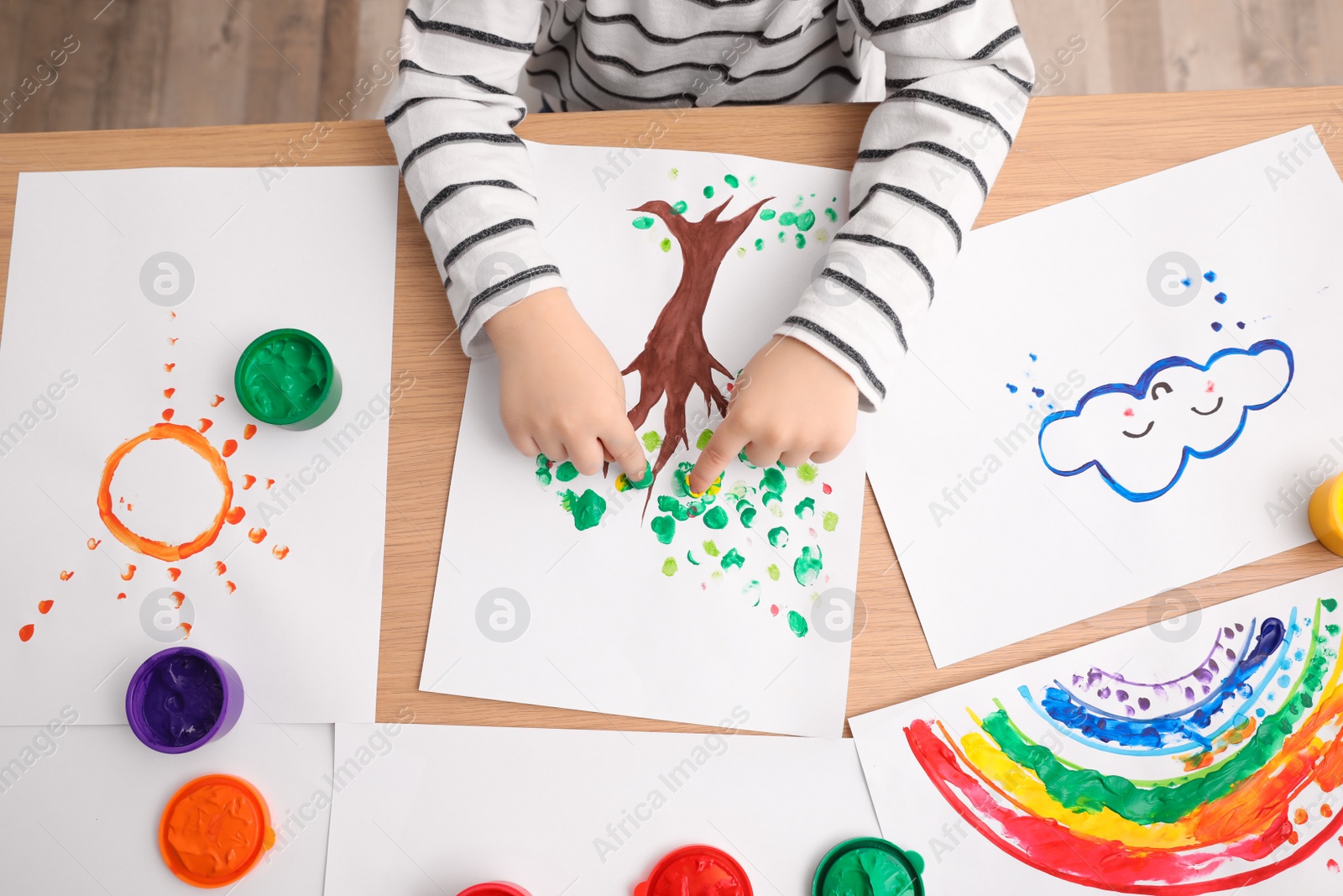 Photo of Little child painting with fingers at wooden table indoors, closeup