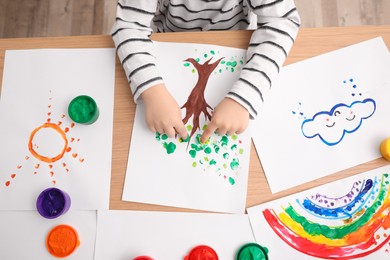 Little child painting with fingers at wooden table indoors, closeup
