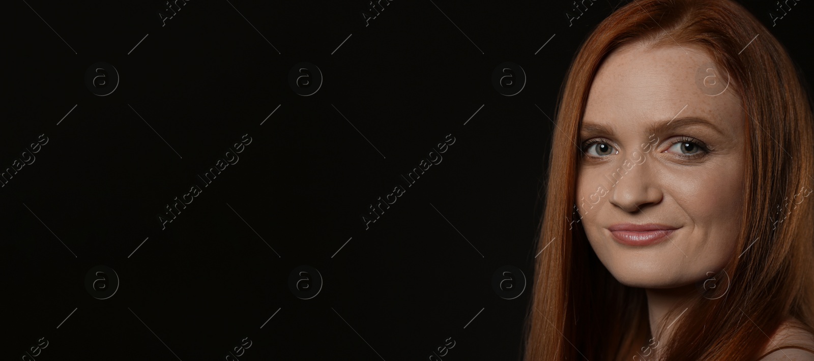 Photo of Candid portrait of happy young woman with charming smile and gorgeous red hair on dark background, space for text