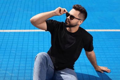 Photo of Handsome man in sunglasses on blue floor covering outdoors, space for text