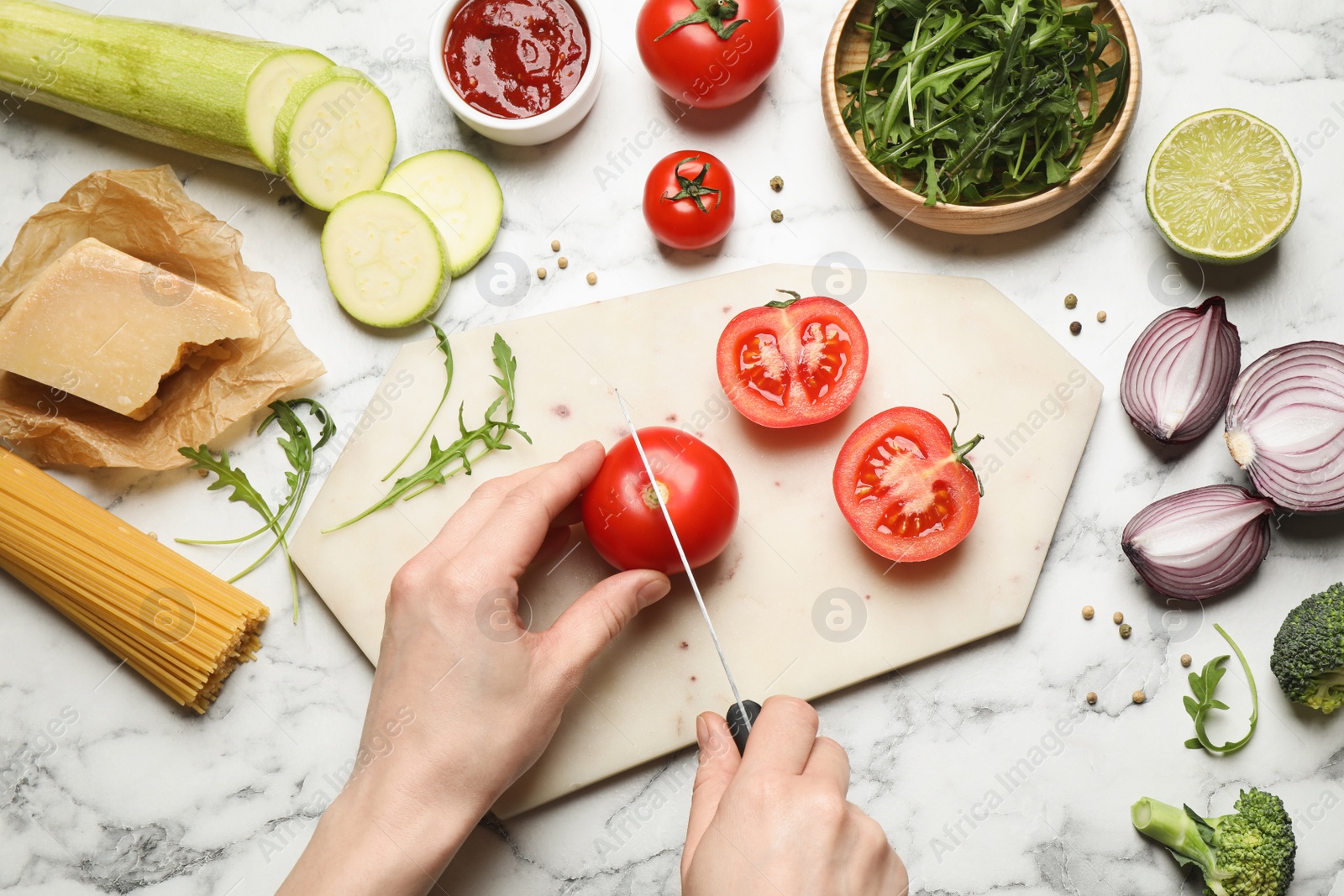 Photo of Woman cutting tomato at marble table, top view. Healthy cooking