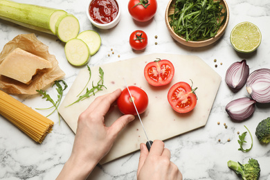 Photo of Woman cutting tomato at marble table, top view. Healthy cooking