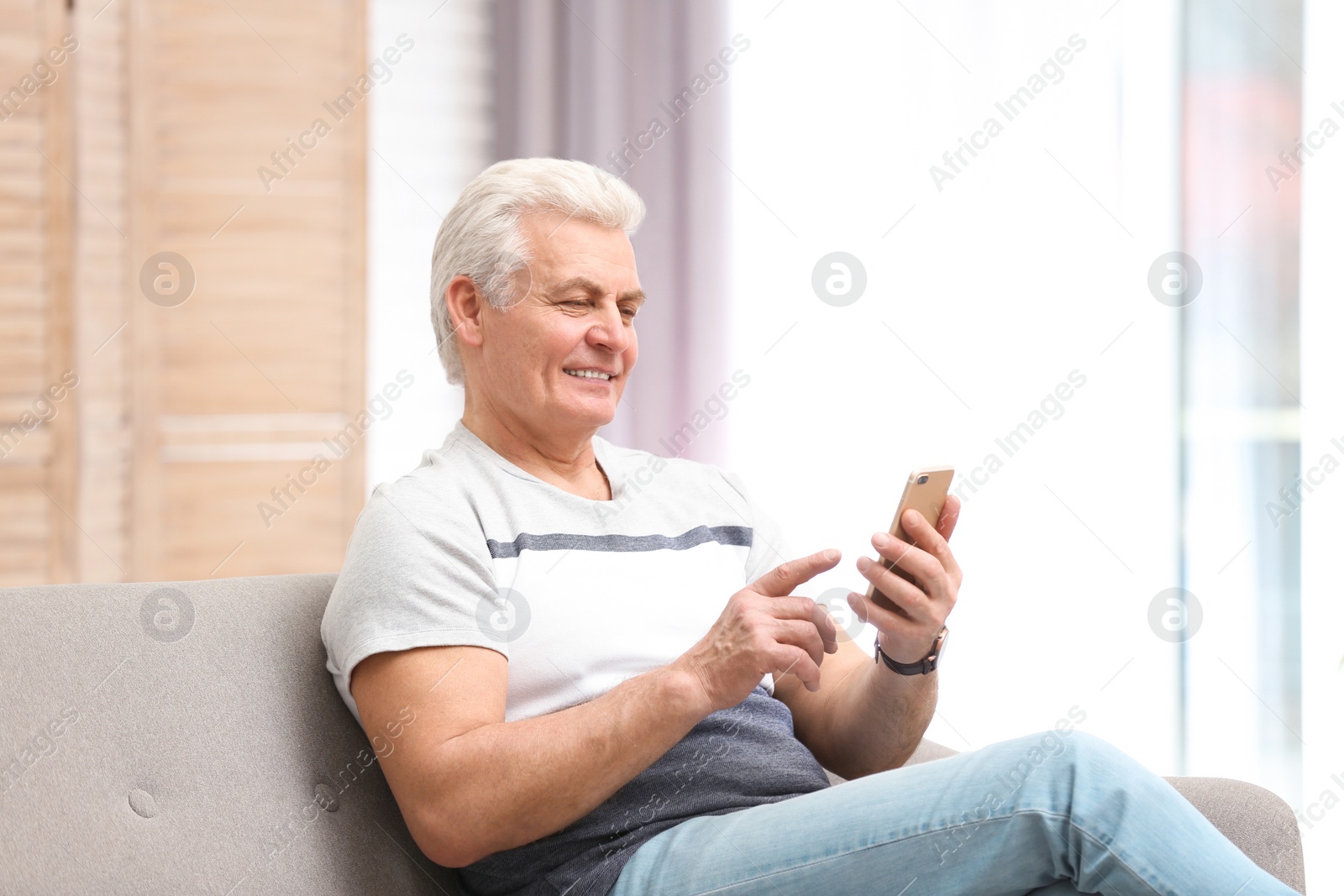 Photo of Portrait of mature man with mobile phone on sofa indoors