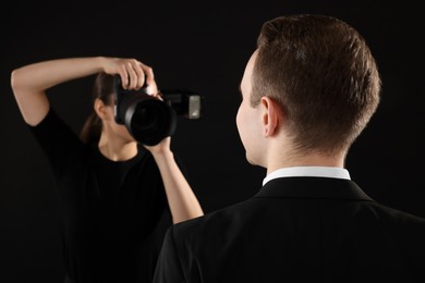 Professional photographer taking picture of man on black background, selective focus