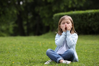 Little girl suffering from seasonal spring allergy on green grass in park. Space for text