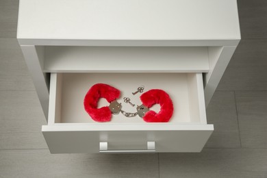 Photo of Red furry handcuffs and keys in drawer indoors, above view. Sex toy