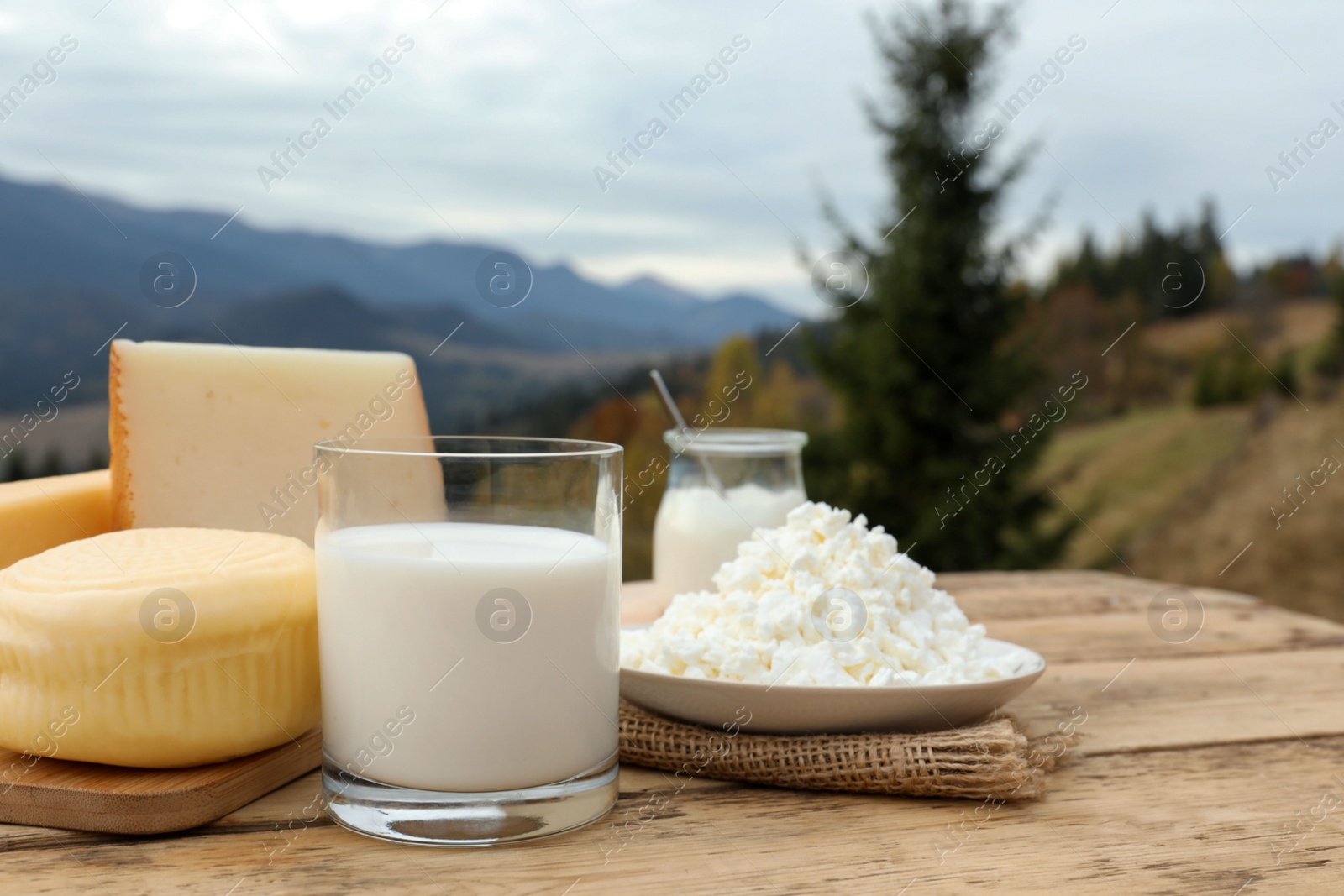 Photo of Tasty cottage cheese and other fresh dairy products on wooden table in mountains