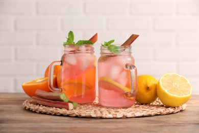 Photo of Mason jars of tasty rhubarb cocktail with citrus fruits on wooden table