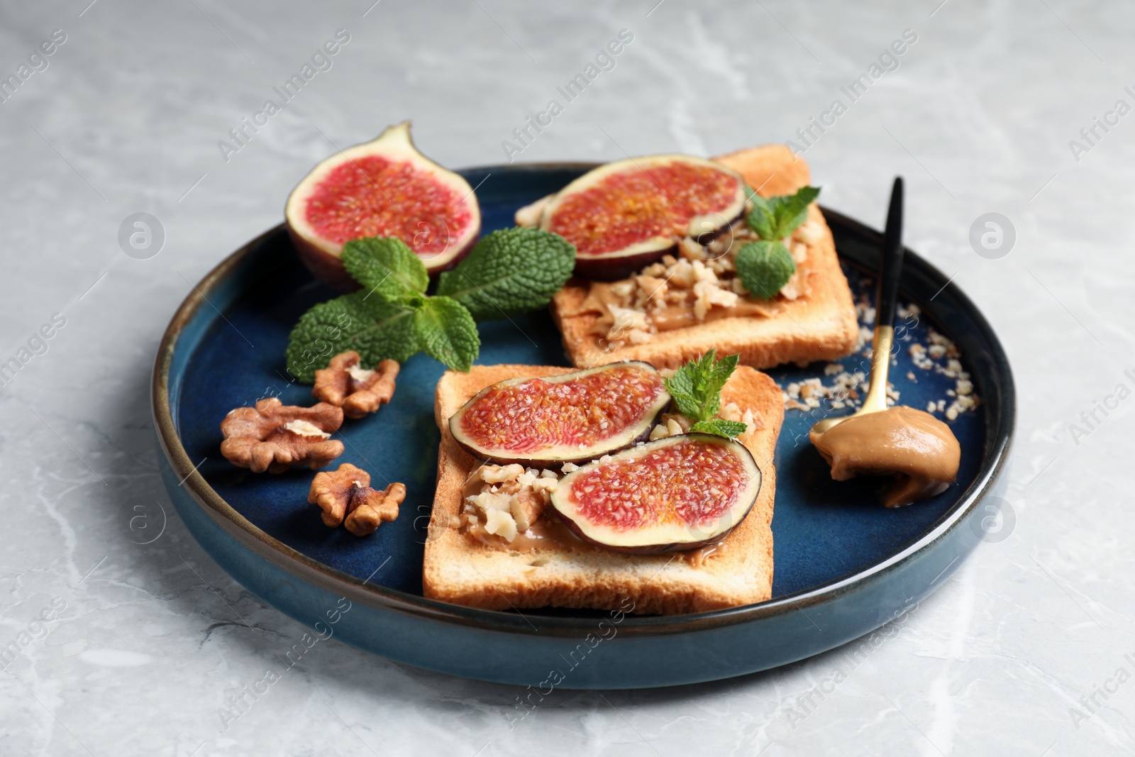 Photo of Tasty toasts served with fig, peanut butter and walnuts on light grey marble table