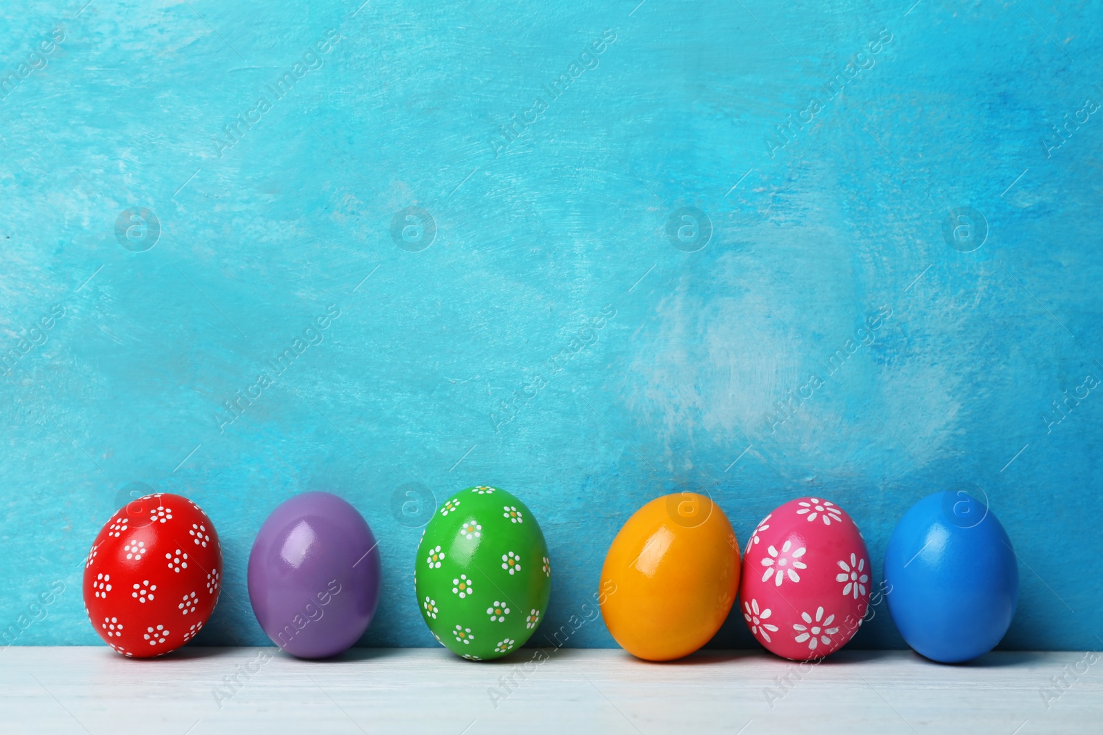 Photo of Decorated Easter eggs on table near color wall. Space for text