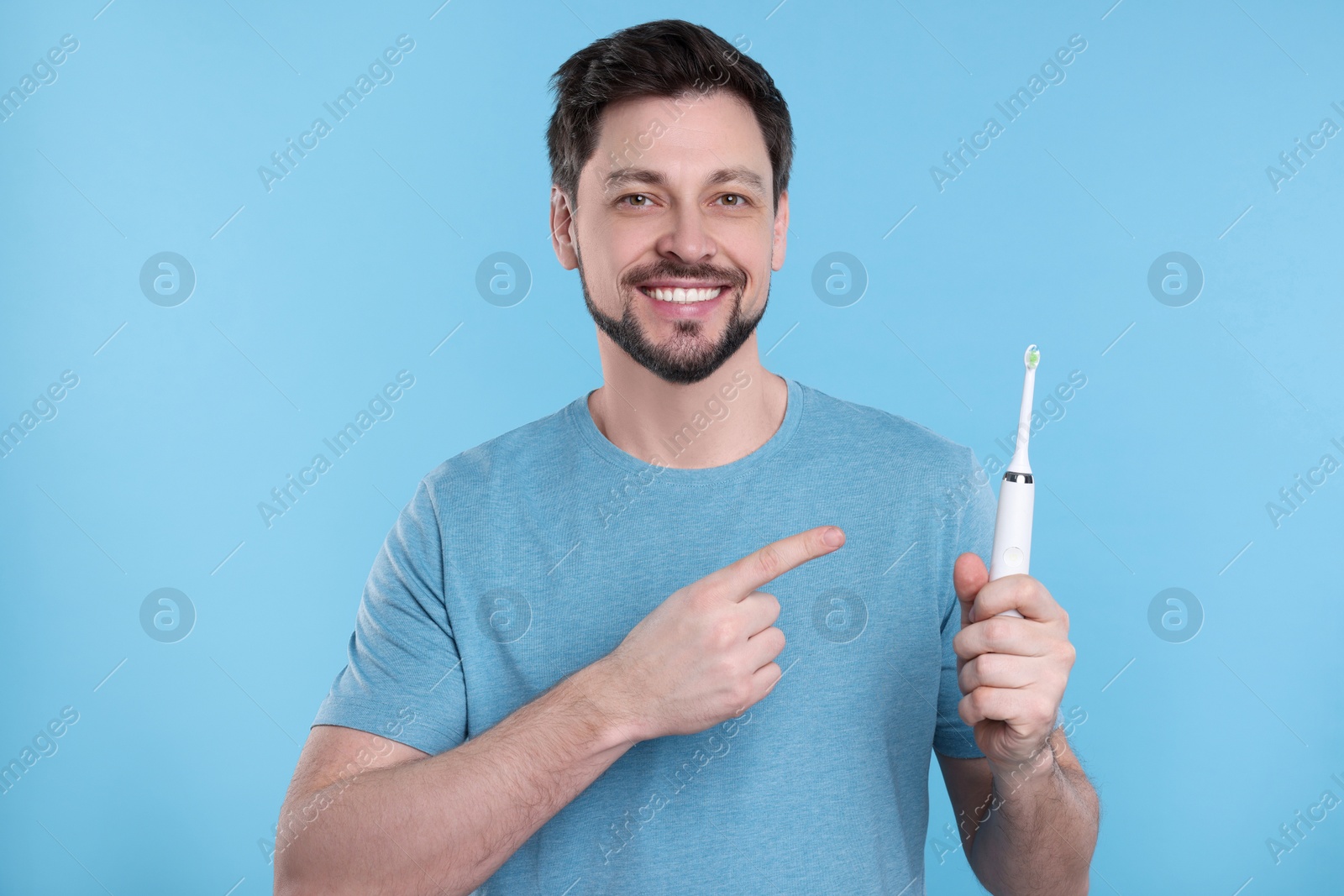 Photo of Happy man holding electric toothbrush on light blue background