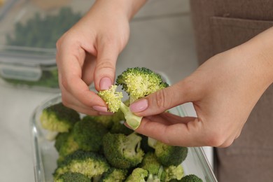 Photo of Woman putting green broccoli into container with fresh vegetables, closeup. Food storage