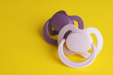 Photo of New baby pacifiers on yellow background. Space for text