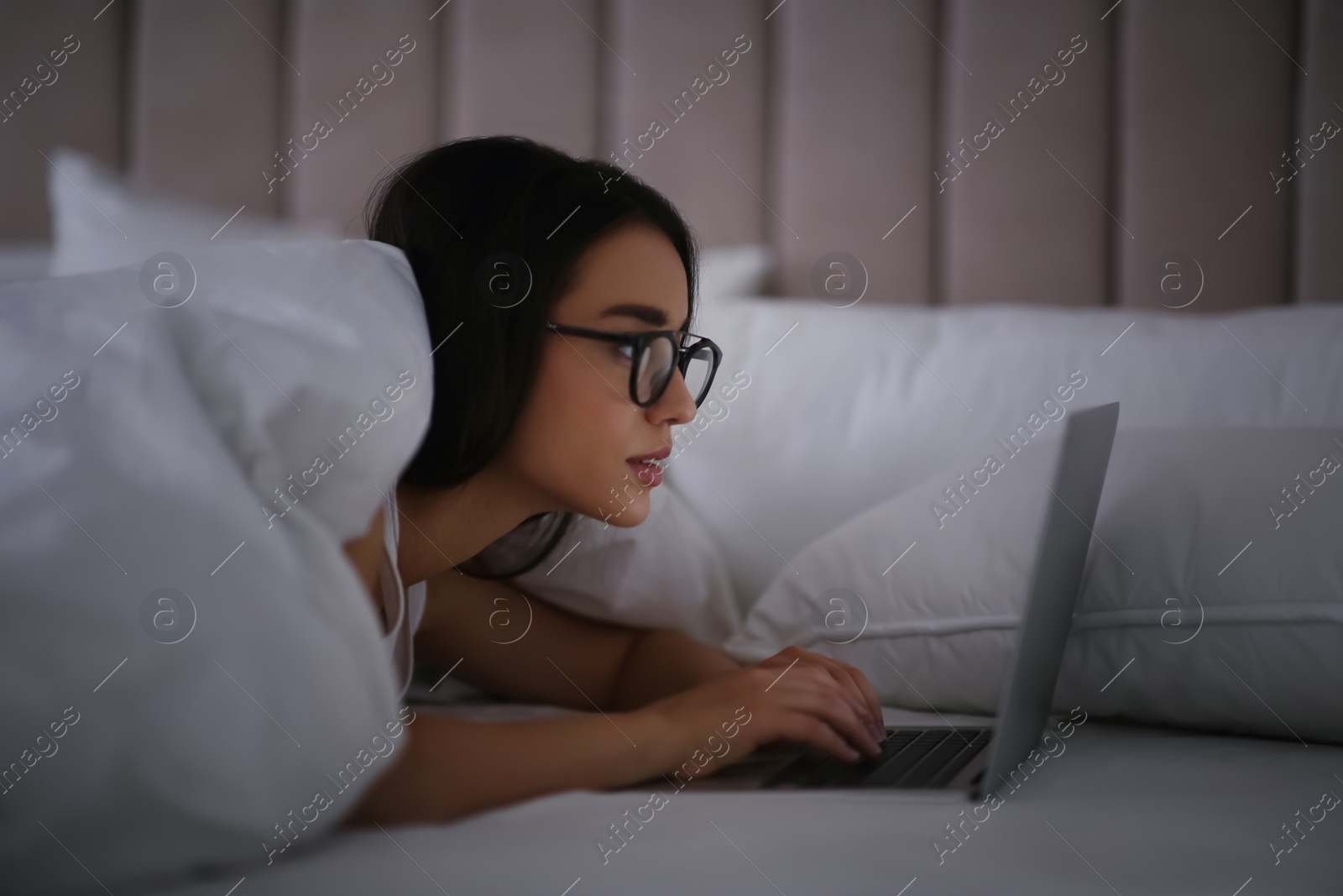 Photo of Young woman with nomophobia using laptop in bed at night. Insomnia concept