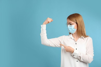 Photo of Woman with protective mask showing muscles on light blue background, space for text. Strong immunity concept