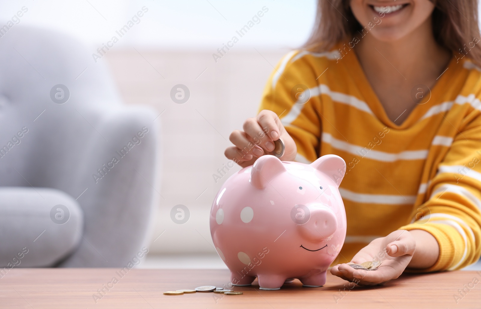 Photo of Woman putting coin into piggy bank at wooden table, closeup. Space for text