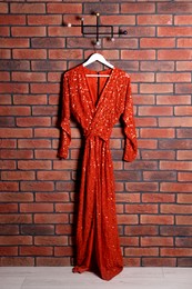 Photo of Beautiful red women's party dress on hanger near brick wall. Stylish trendy clothes for high school prom