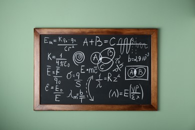 Photo of Blackboard with different physical formulas written with chalk on light green wall