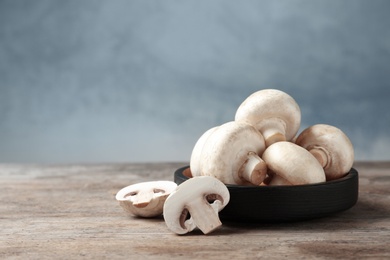 Photo of Fresh champignon mushrooms and plate on wooden table, space for text