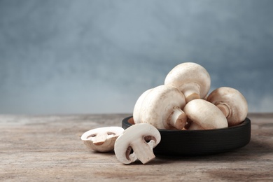 Fresh champignon mushrooms and plate on wooden table, space for text