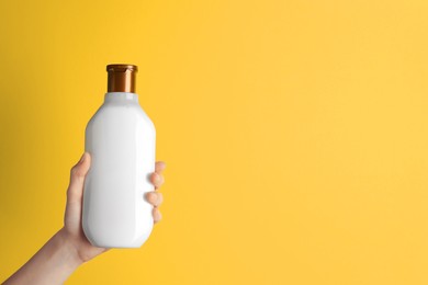 Photo of Woman holding shampoo bottle on yellow background, top view. Space for text