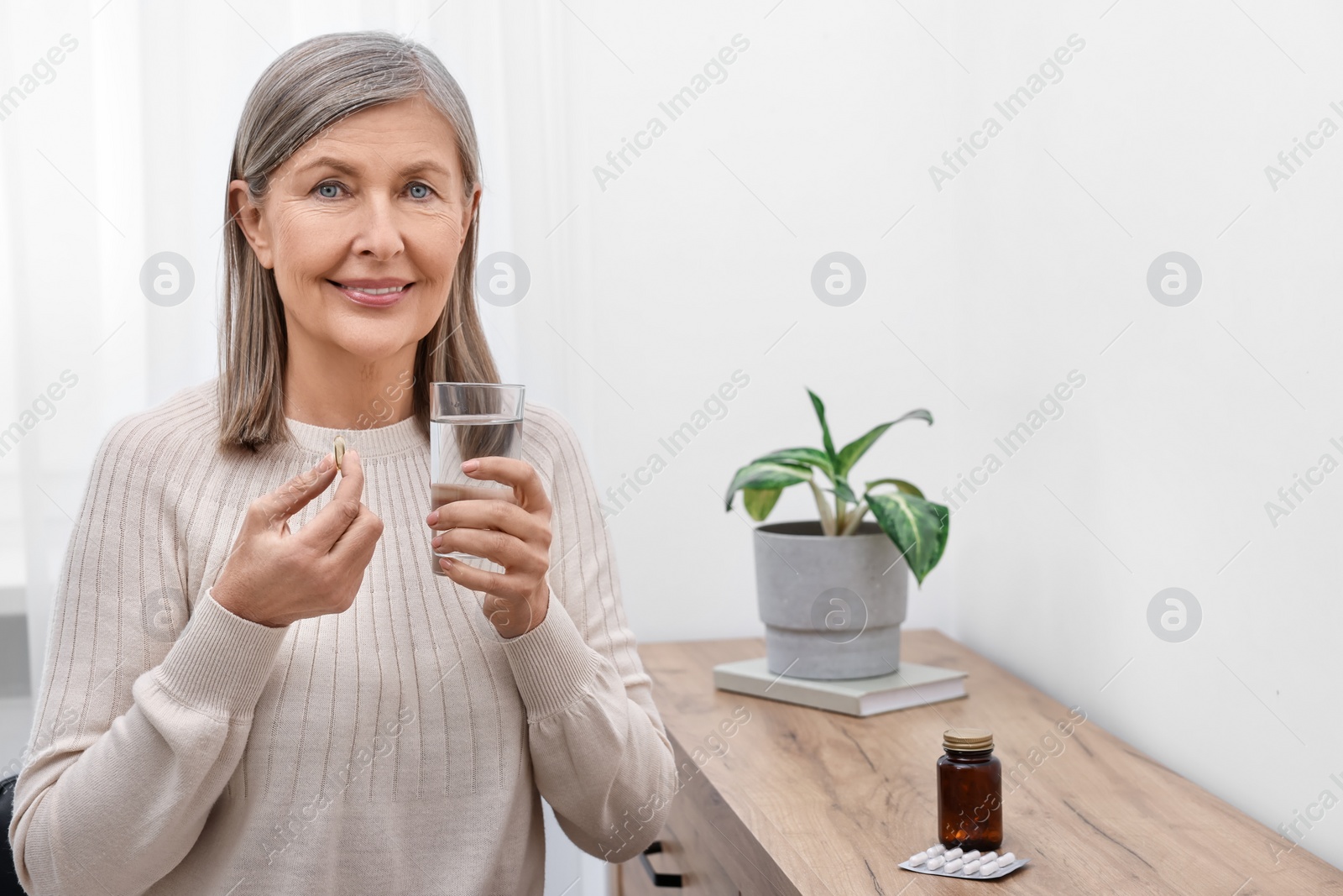 Photo of Beautiful woman taking vitamin pill at table indoors. Space for text