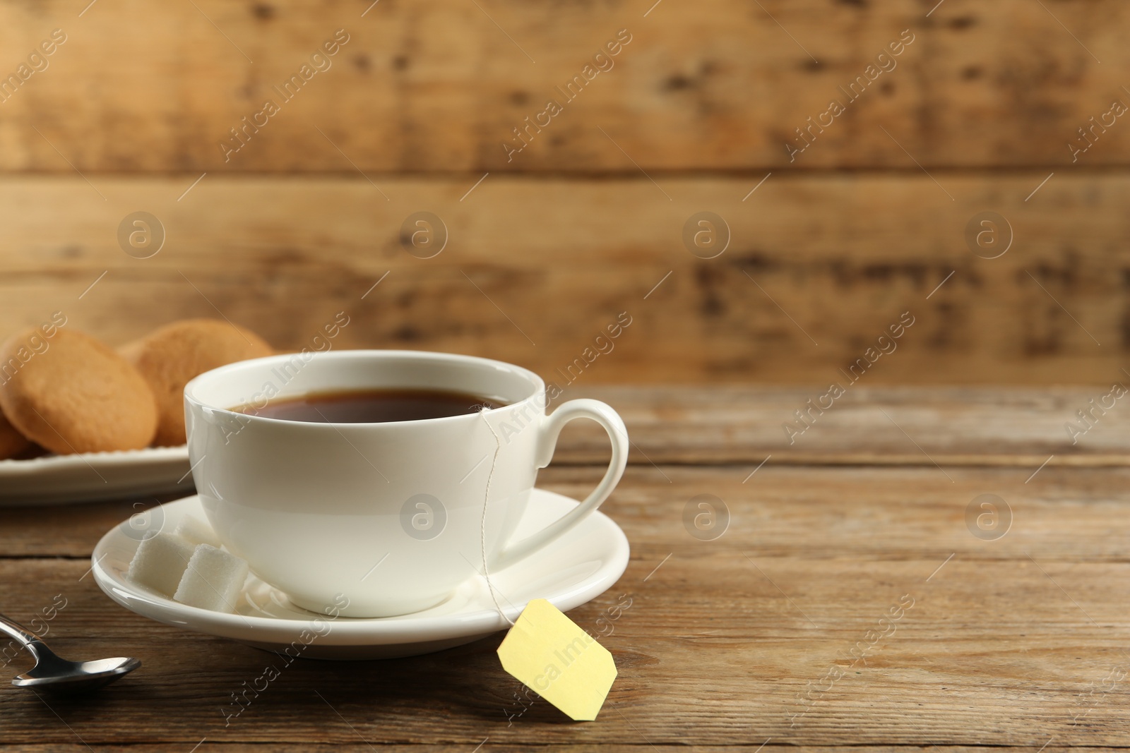 Photo of Tea bag in ceramic cup of hot water on wooden table. Space for text