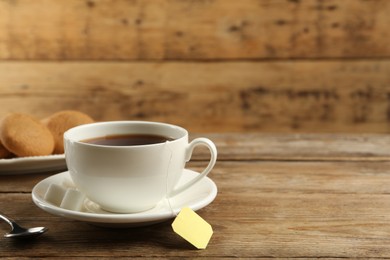 Photo of Tea bag in ceramic cup of hot water on wooden table. Space for text