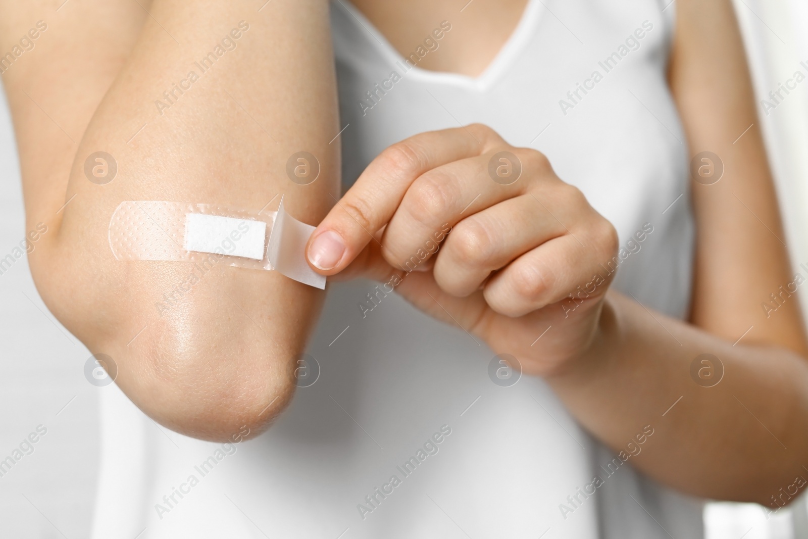 Photo of Female applying plaster on elbow against white background, closeup view