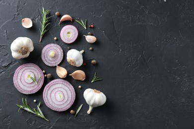 Fresh raw garlic, onion rings and spices on black table, flat lay. Space for text