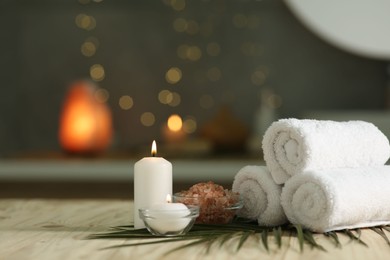 Photo of Spa composition. Rolled towels, sea salt and burning candles on table against blurred lights, space for text