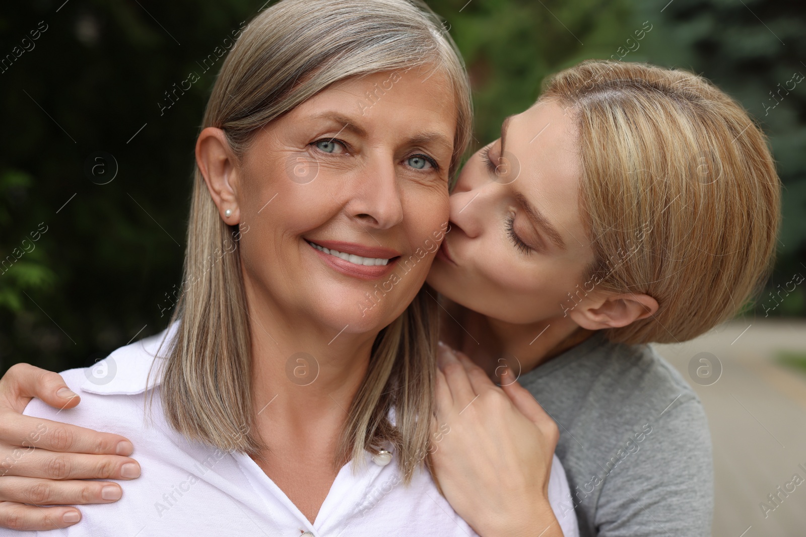 Photo of Daughter kissing her mature mother on cheek outdoors