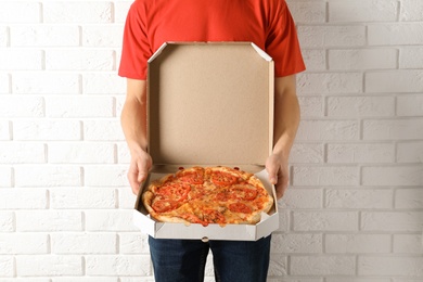 Photo of Young man with opened pizza box near white brick wall. Food delivery service