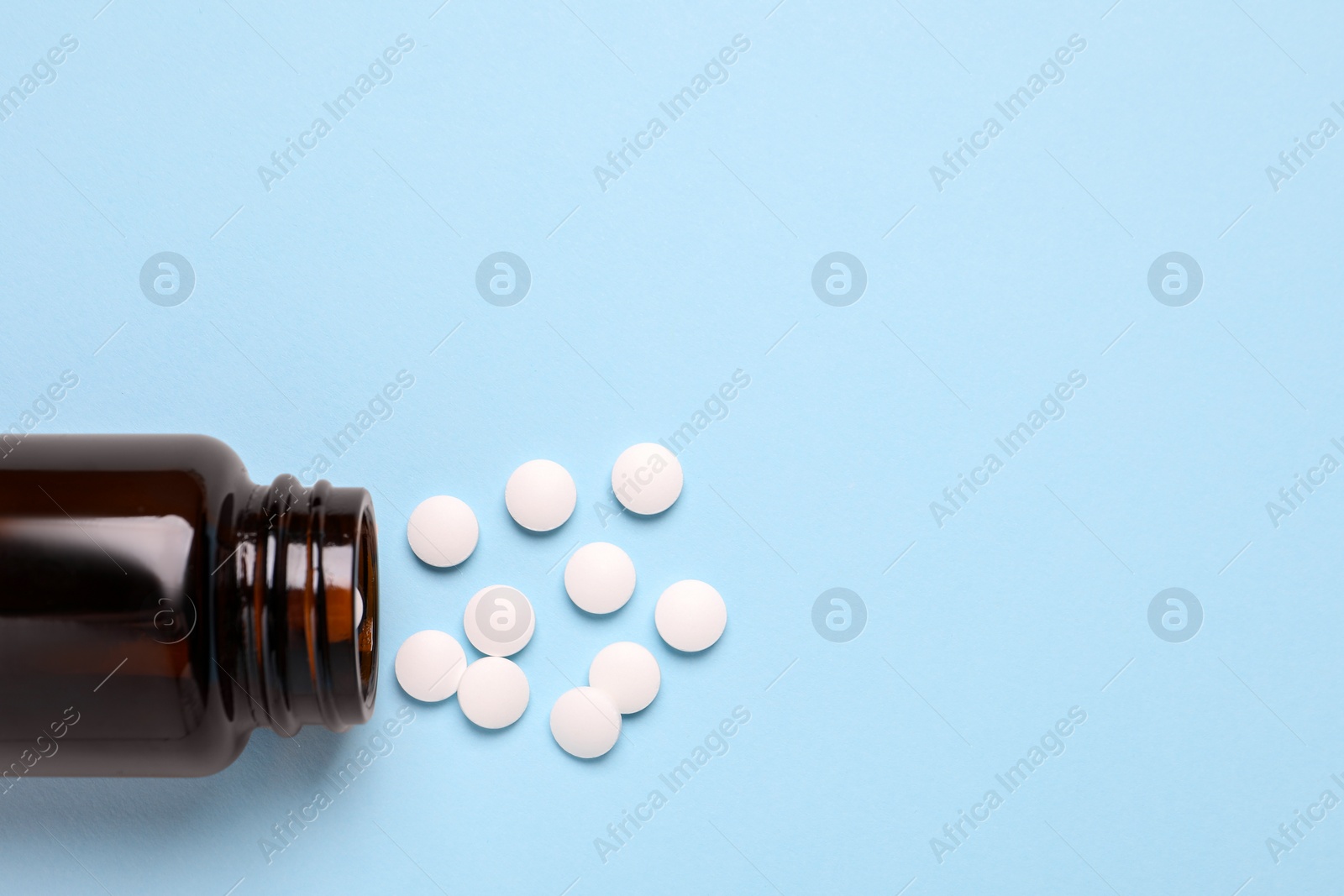 Photo of Plastic medical bottle with pills on light blue background, flat lay. Space for text