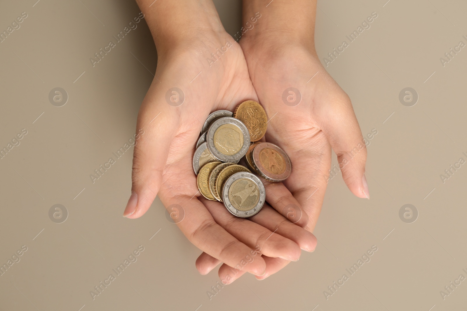 Photo of Young woman with handful of coins on beige background, top view